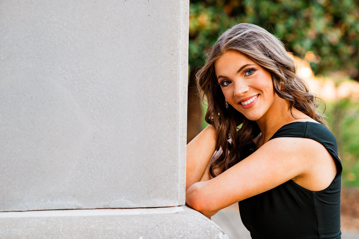 College senior in black dress smiling at camera on MTSU campus