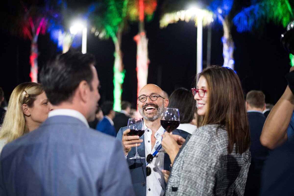 Outdoor reception showing people holding red wine and laughing