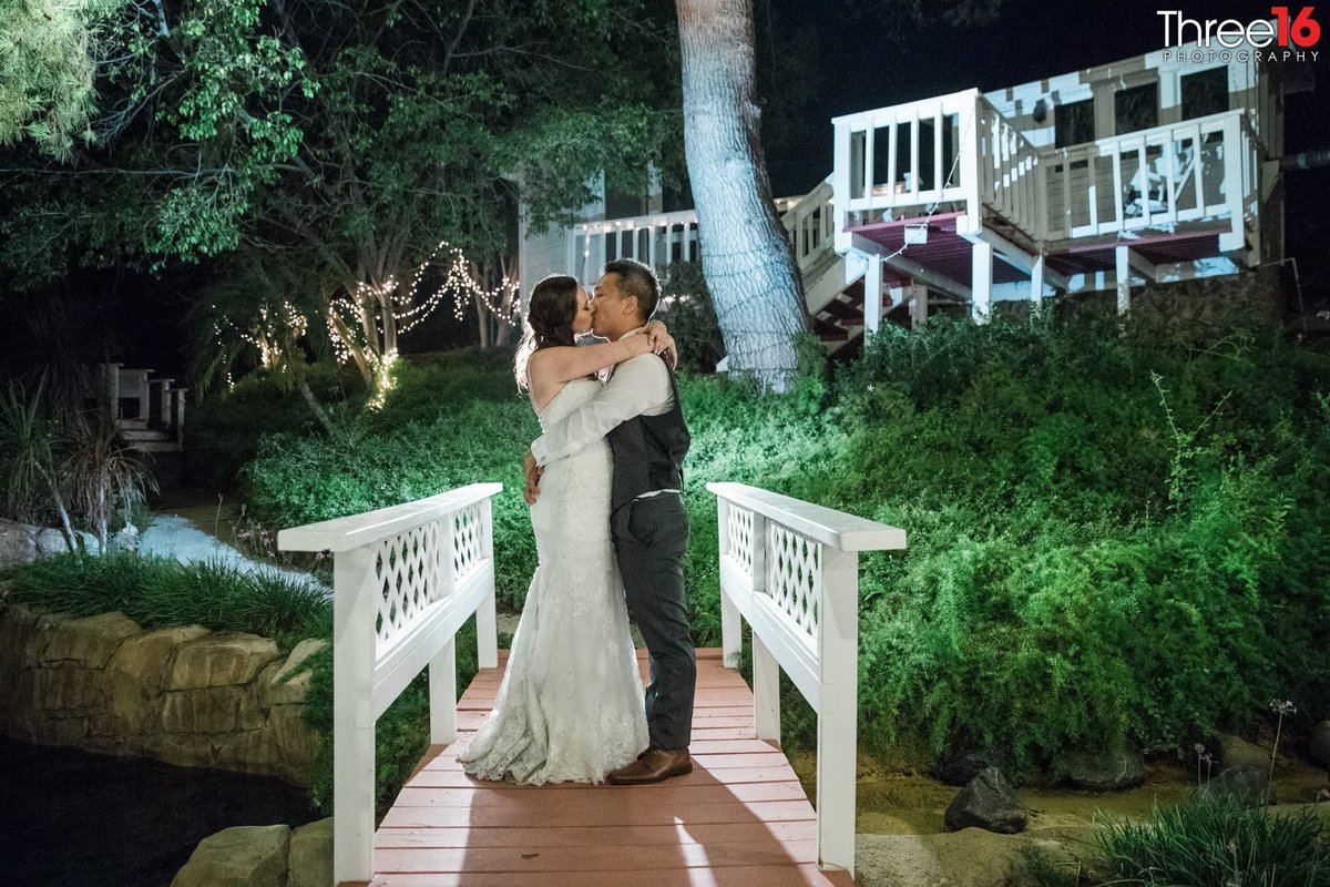 Newly married couple spend a moment alone kissing on the pond bridge at night