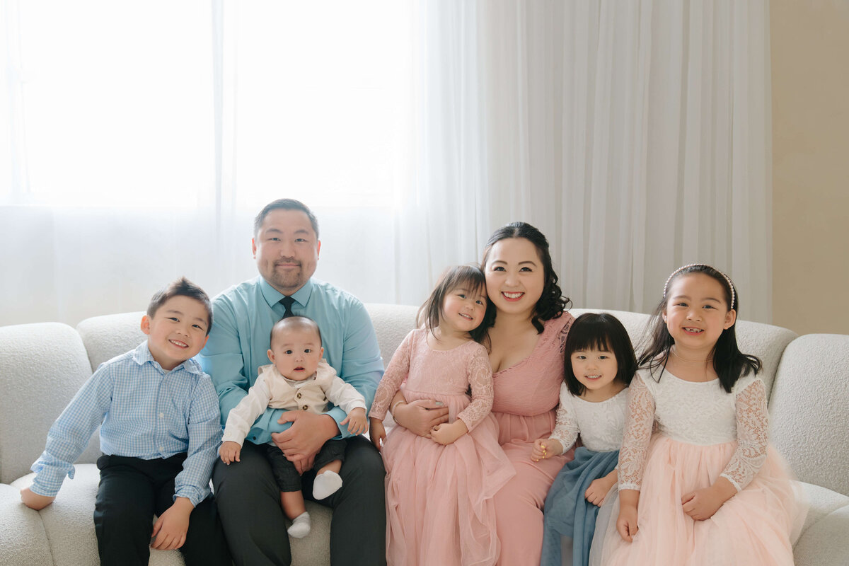 A family sits comfortably on a couch, with their children nestled beside them, creating a warm and joyful atmosphere.