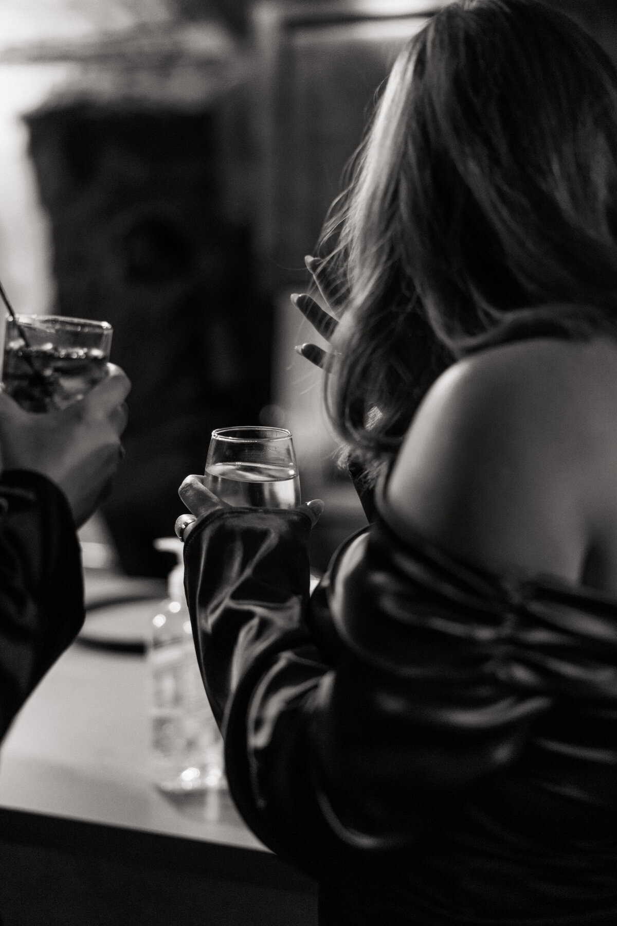 Moody black-and-white shot of a woman holding drinks at a bar during a Philadelphia wedding celebration.