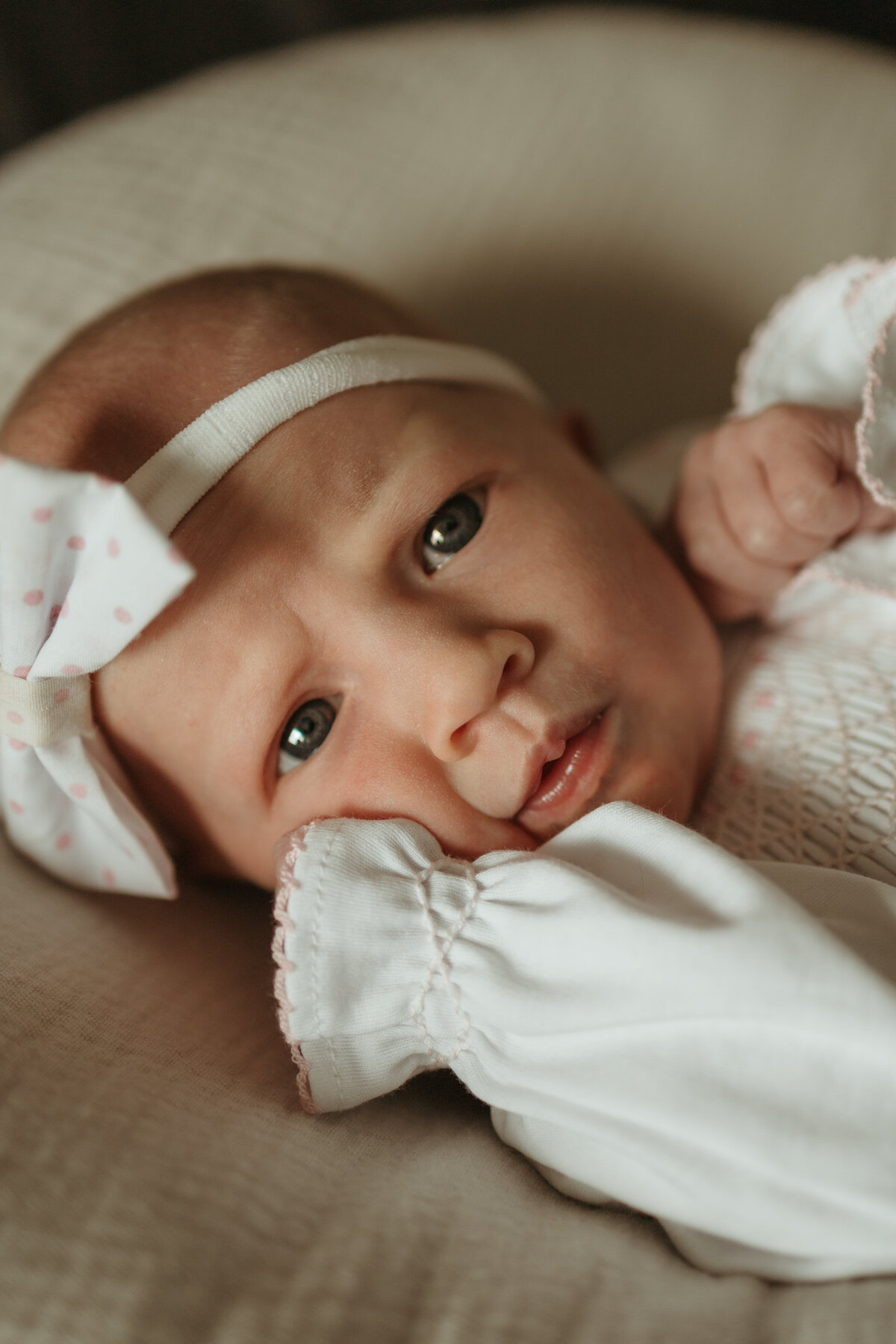 Newborn baby in Firestone Colorado during in home newborn session wearing a white baby gown with white polka dot bow