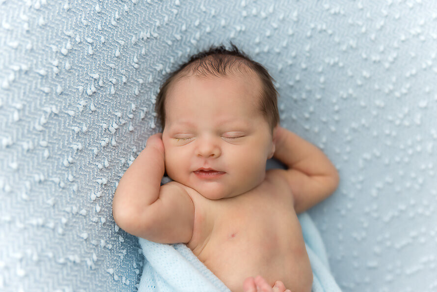 Baby boy sleeps on back on a blue backgrop.