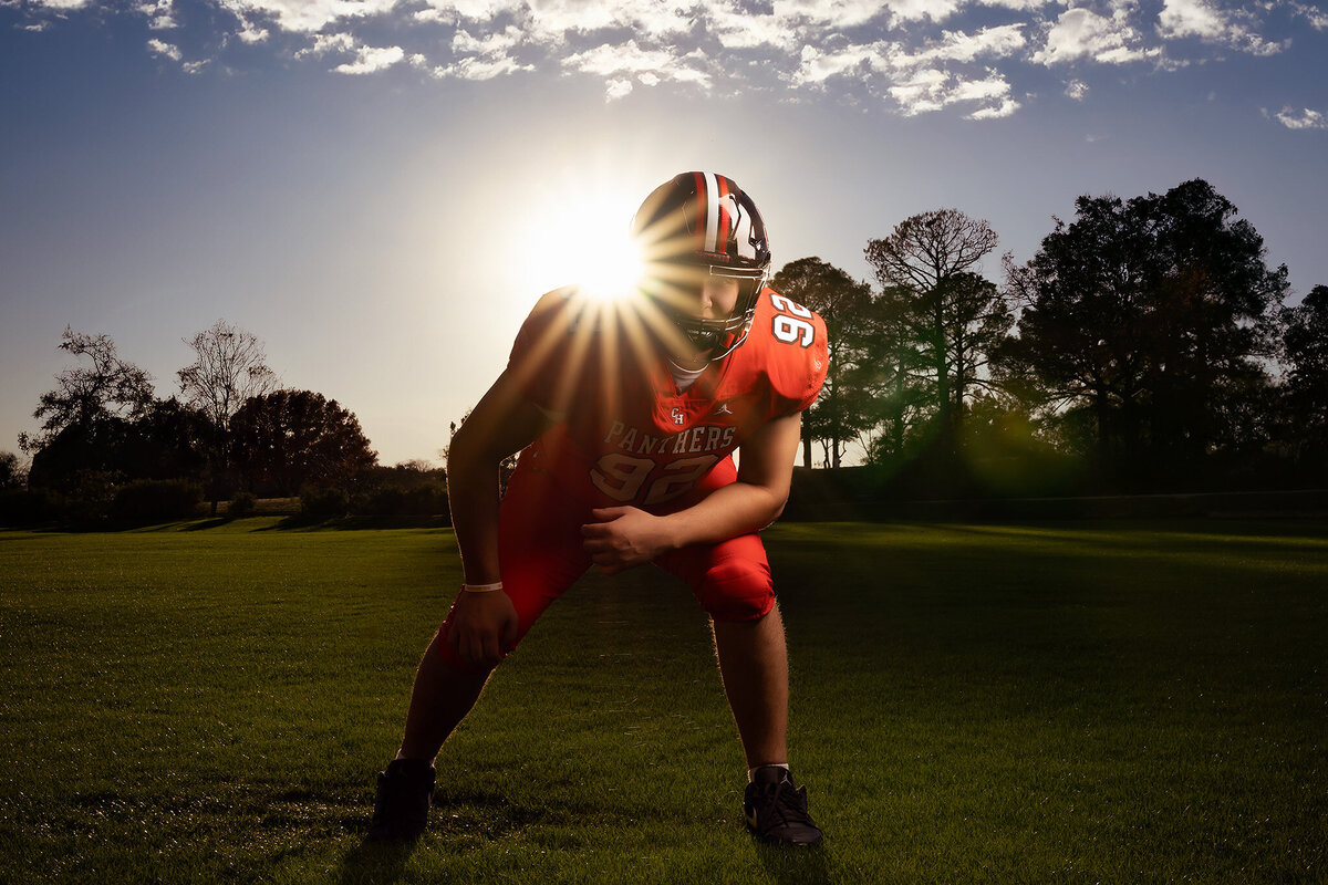 Dallas senior photographer captures an athlete in football gear, poised on the field with the sun setting behind him. The dynamic image blends senior photography with a dramatic lighting effect, ideal for those seeking high-energy, impactful senior portraits in Dallas. The photo showcases a unique sports-inspired style perfect for your senior photo session.