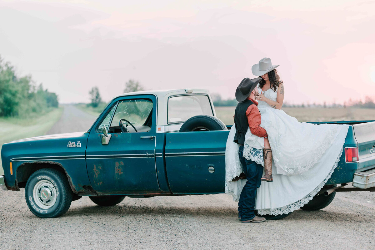 Bride sits on top of truck box and groom faces her. 
