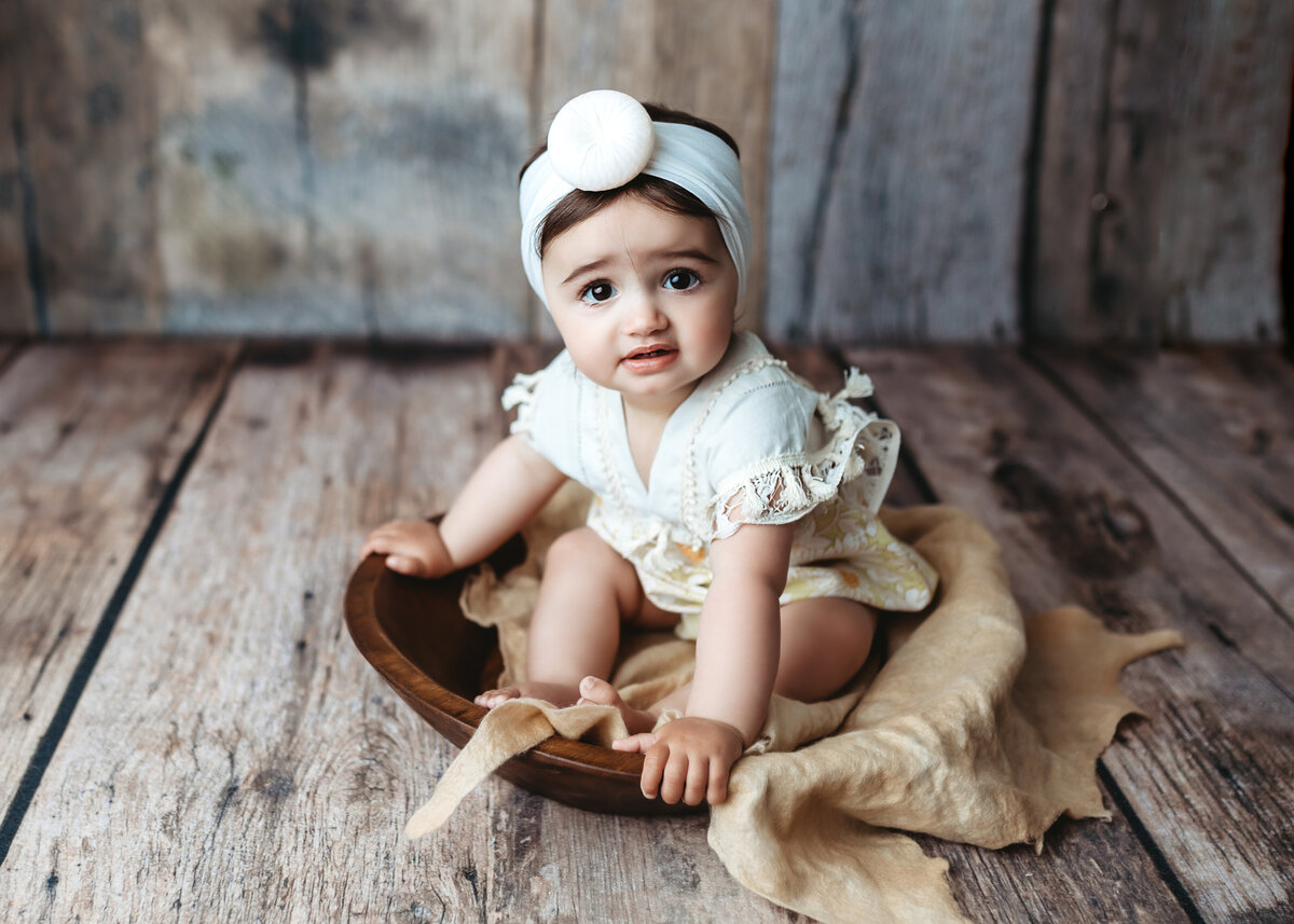 adorable baby girl sits in bowl for photo in Denver photography studio for toddler sitter photoshoot