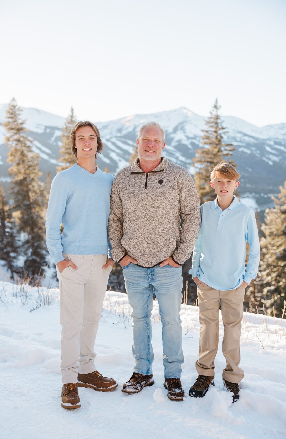 A happy dad stands on a mountain overlook with his two teen sons