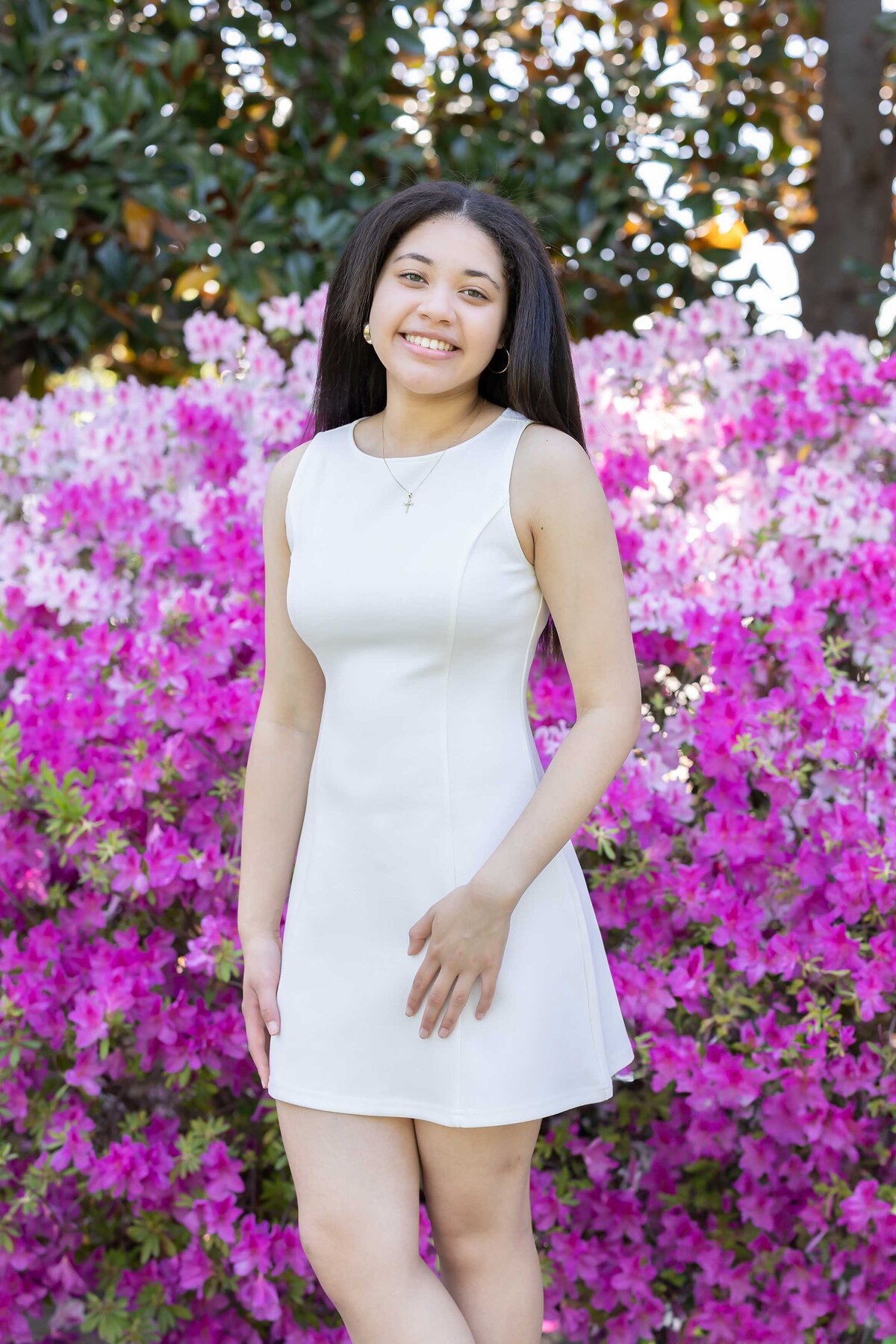 Custom senior photo experience featuring a beautiful girl in a white dress with a pink floral background at her school, part of the Senior Photography Portfolio.