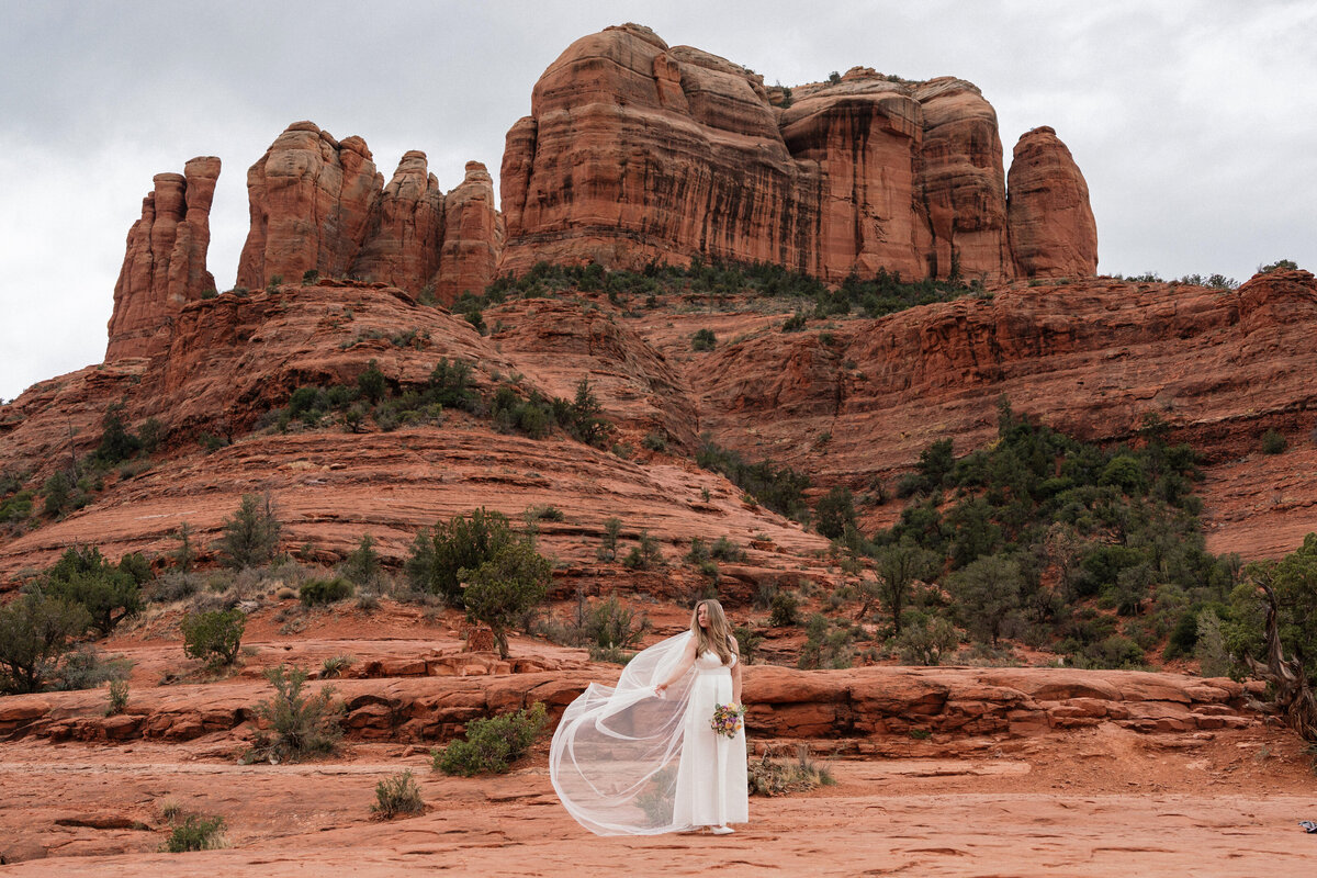 Bride holding bouquet with flowing veil during Sedona elopement at Cathedral Rock, surrounded by red rock formations and desert landscape