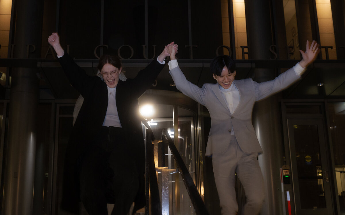 The couple, filled with happiness, lifts their arms in celebration outside the Seattle Courthouse after their wedding ceremony, embracing their new journey together.