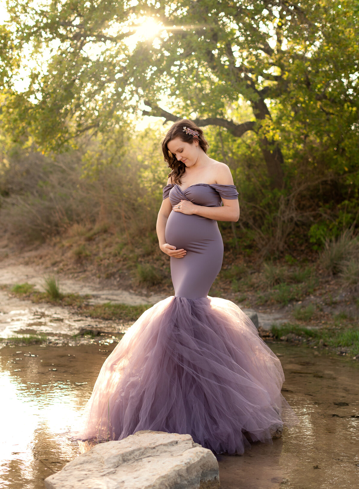 Pregnant woman wearing a purple fitted dress with tulle in a creek