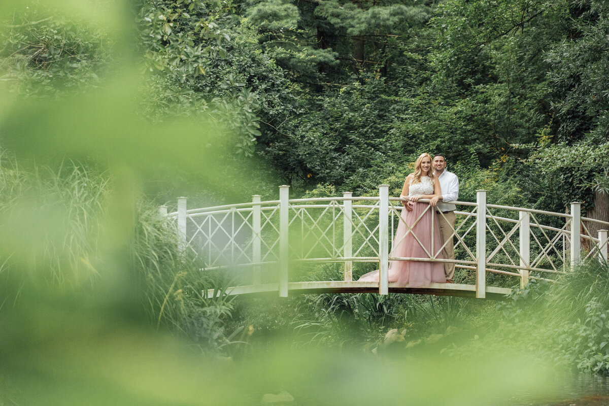 Couple by white bridge during summer engagement session at Sayen House and Gardens in Hamilton Township New Jersey