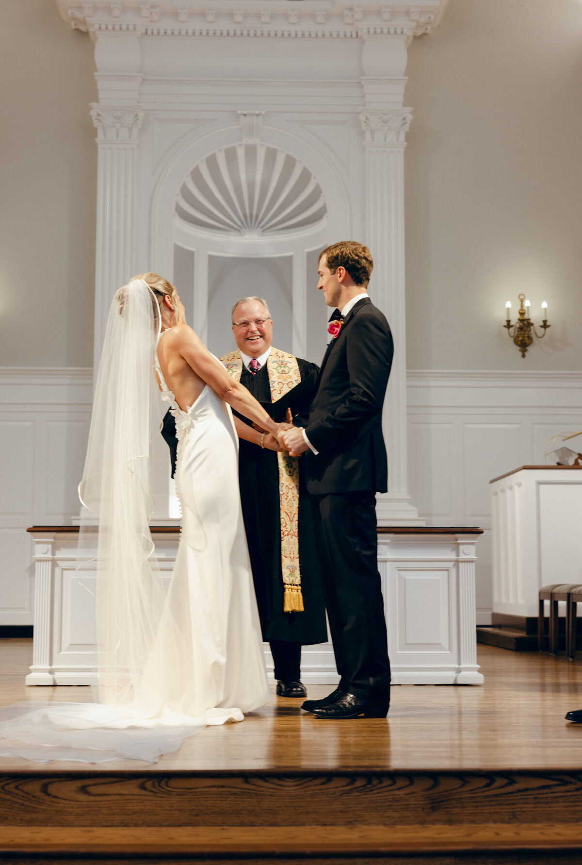 A wedding day photo of the bride and groom holding hands while standing at the alter