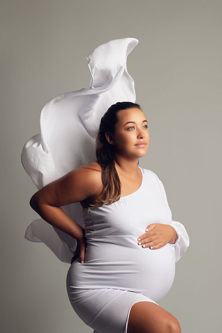 Pregnant woman holding bump on grey backdrop