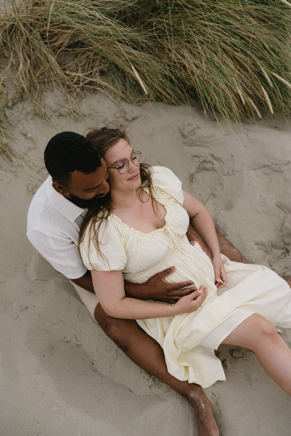 Foto van koppel dat een kindje verwacht en in de duinen zit.