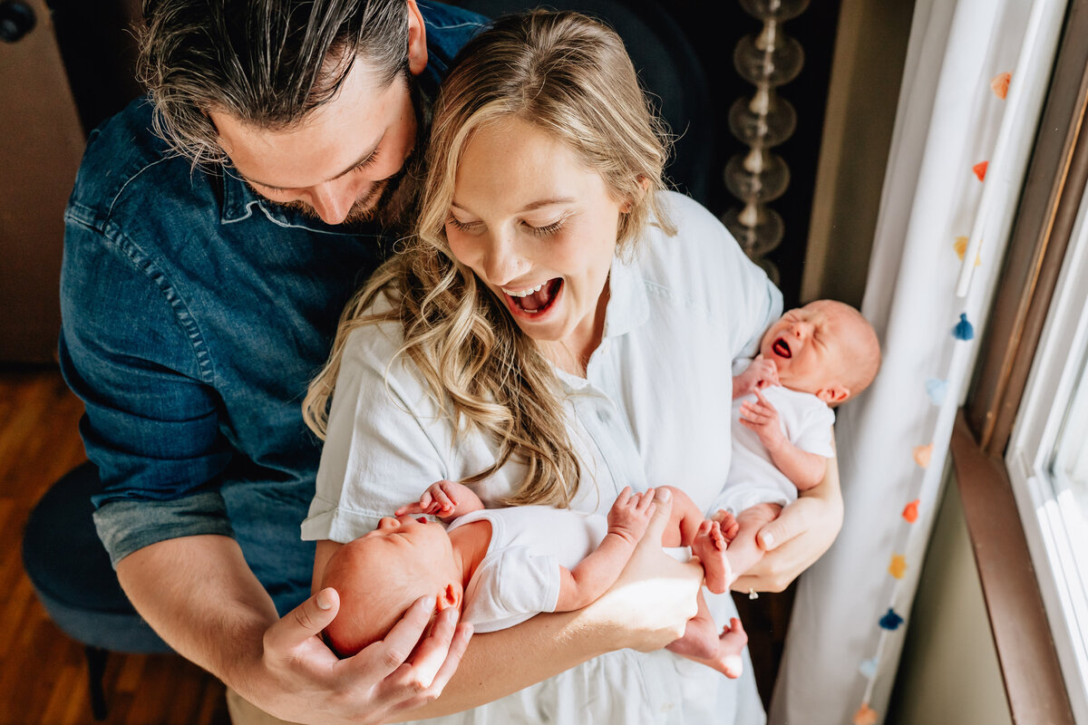 A close-up color image of a mother and father standing close together, each holding one of their newborn twins.