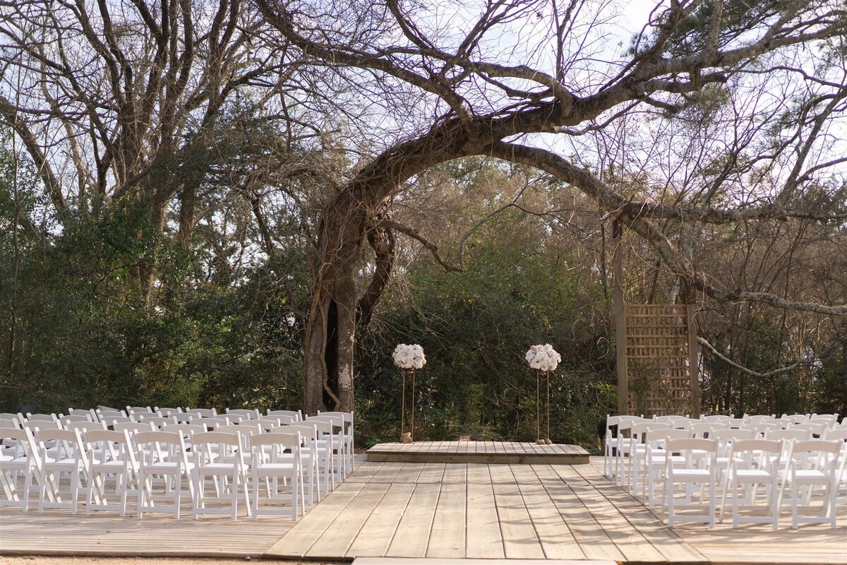 Wedding ceremony with white chairs and 2 lifted floral arrangements.