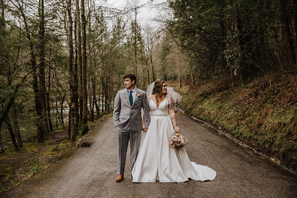 Bride and groom standing hand in hand on a wooded road near Greenbrier, looking in opposite directions during their eloping to Gatlinburg wedding.
