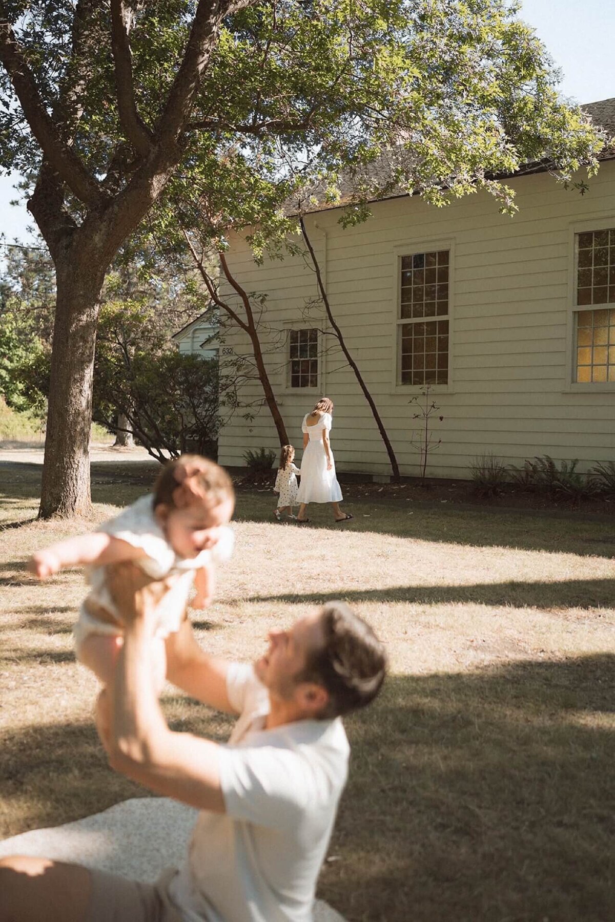 father holding up baby with mother and daughter in background at so cal park