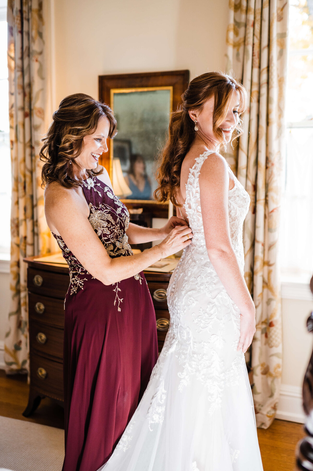 maid of honor helps button up the brides wedding dress in a bridal suite of a Charlottesville wedding venues with bride smiling over her shoulder