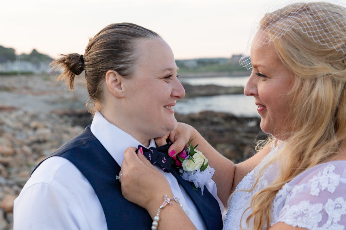 Brides adjusting bow tie at beach