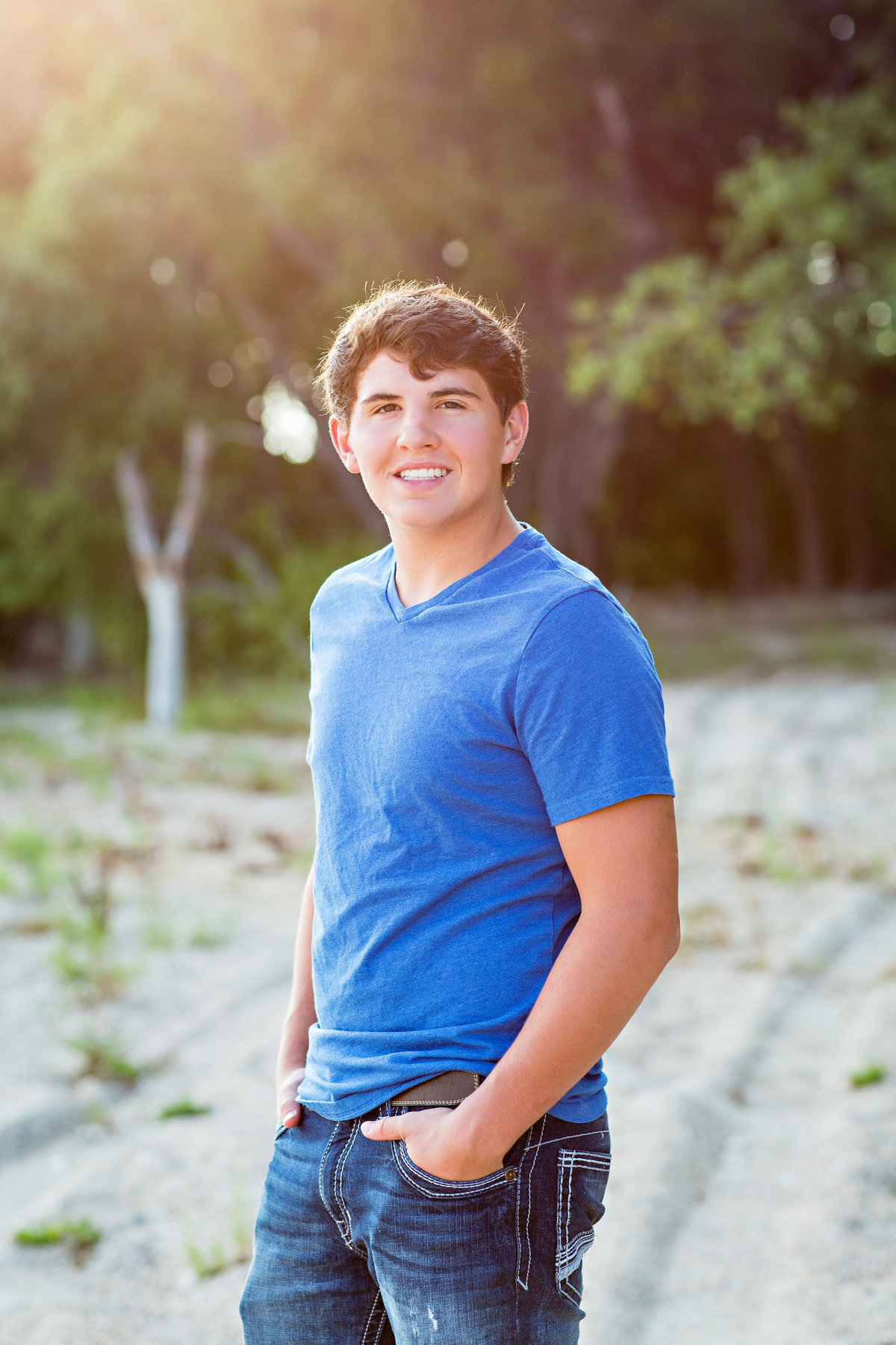 Smiley senior boy in a blue shirt on the beach at sundown