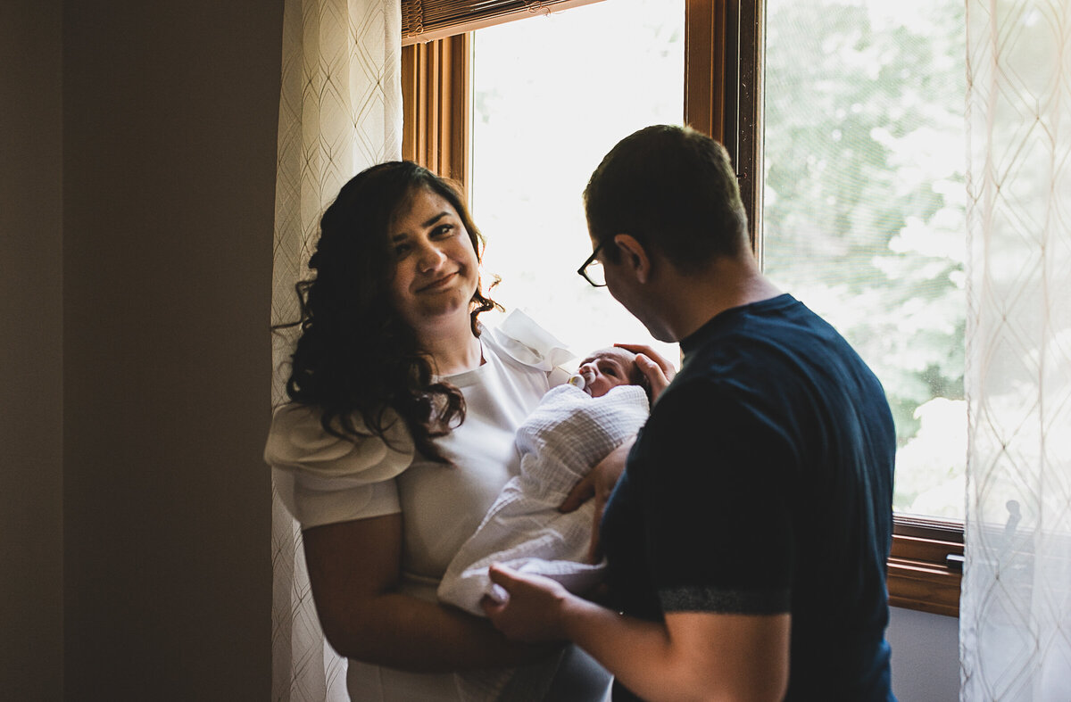 Mom holding new born baby, with dad holding arms around mom.