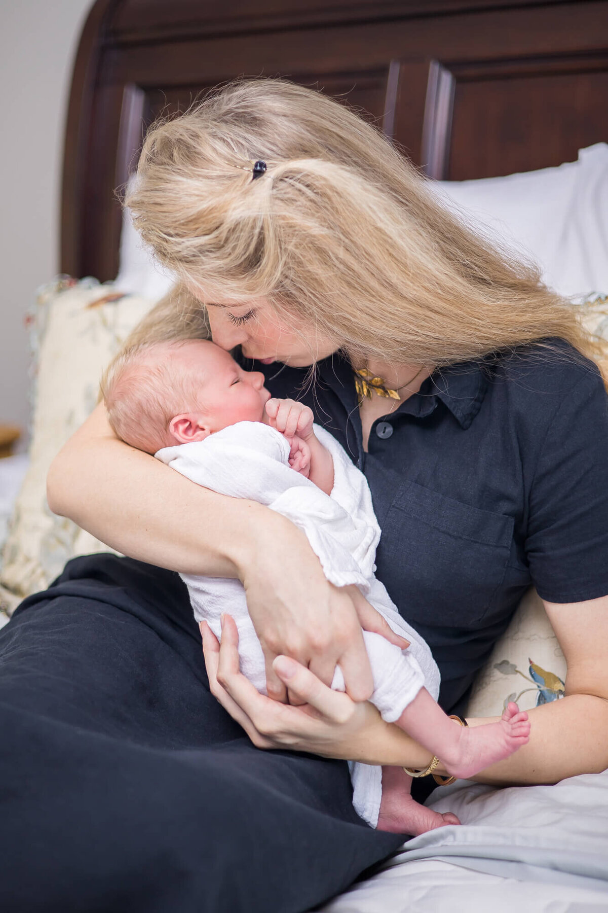 new mom kissing her newborn son while snuggling on the bed