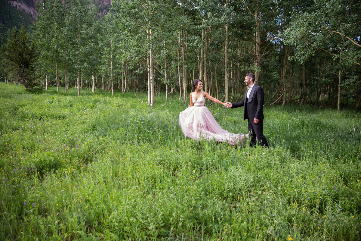 Bride leads her groom in a tree-lined field
