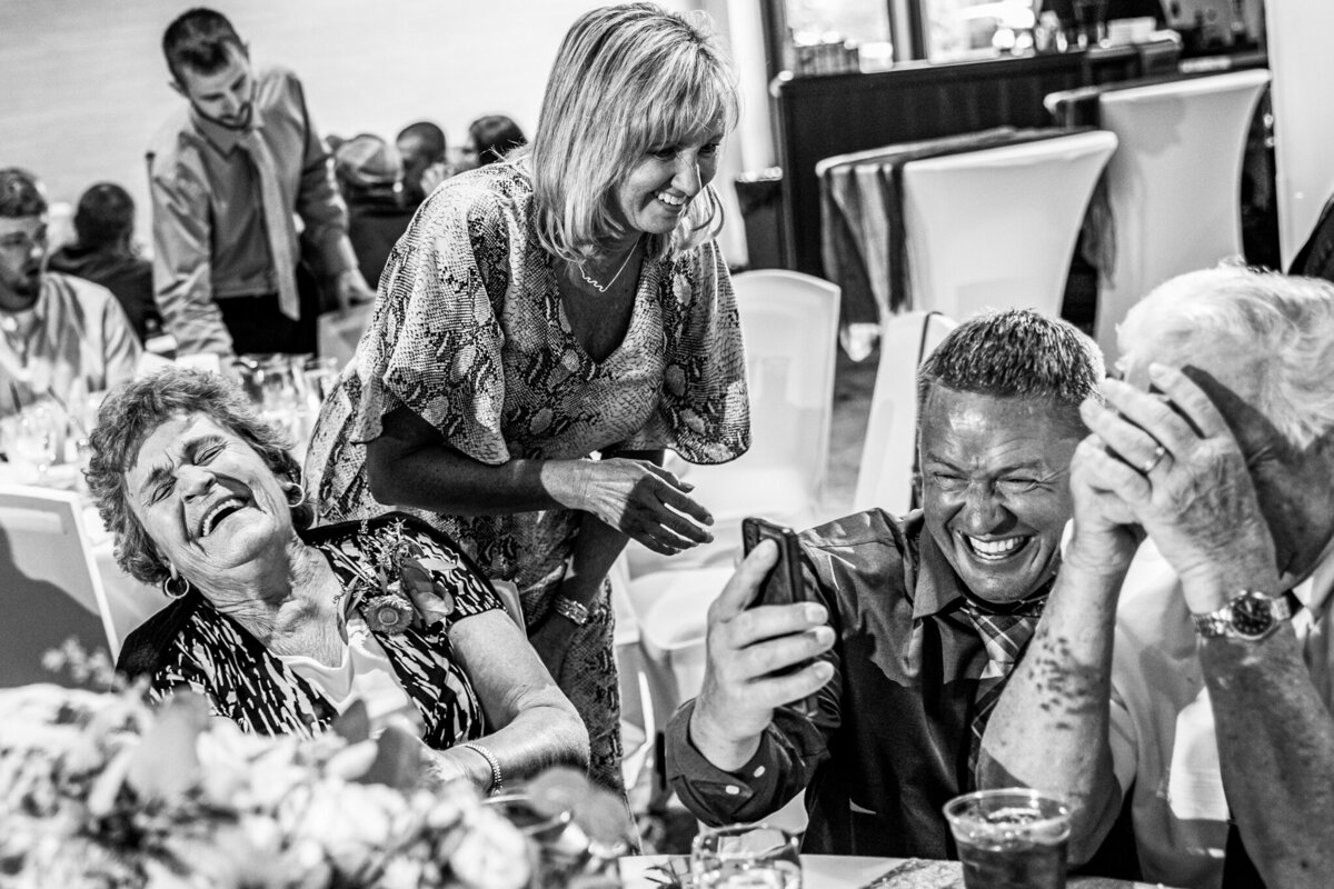 Wedding guest at a table burst our laughing looking at a phone.