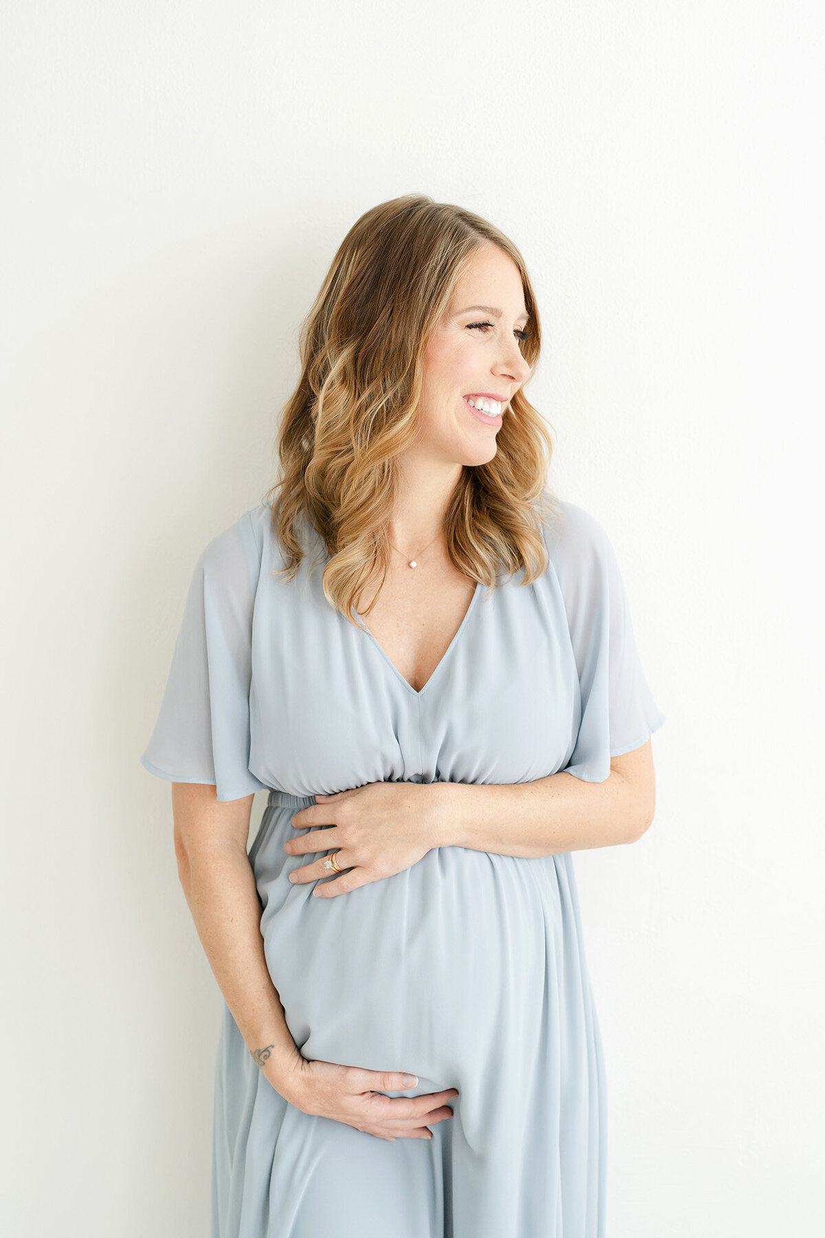 Mom in blue dress holding pregnant belly by Louisville maternity photographer