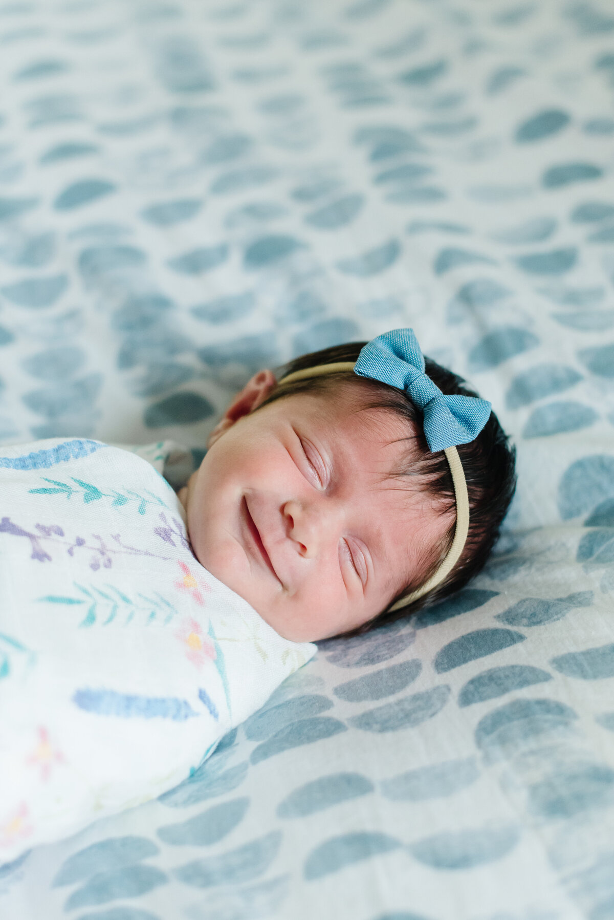 Baby girl swaddled on blue and white blanket smiling