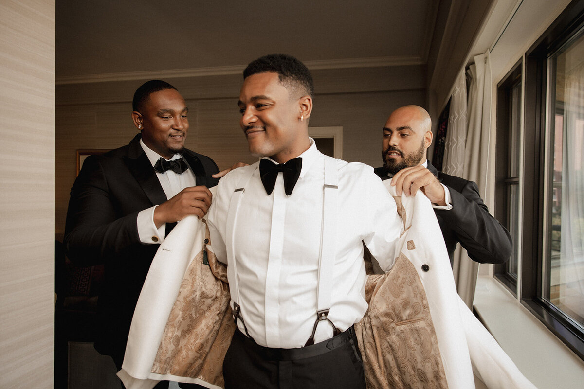 black groom putting jacket on for wedding ceremony