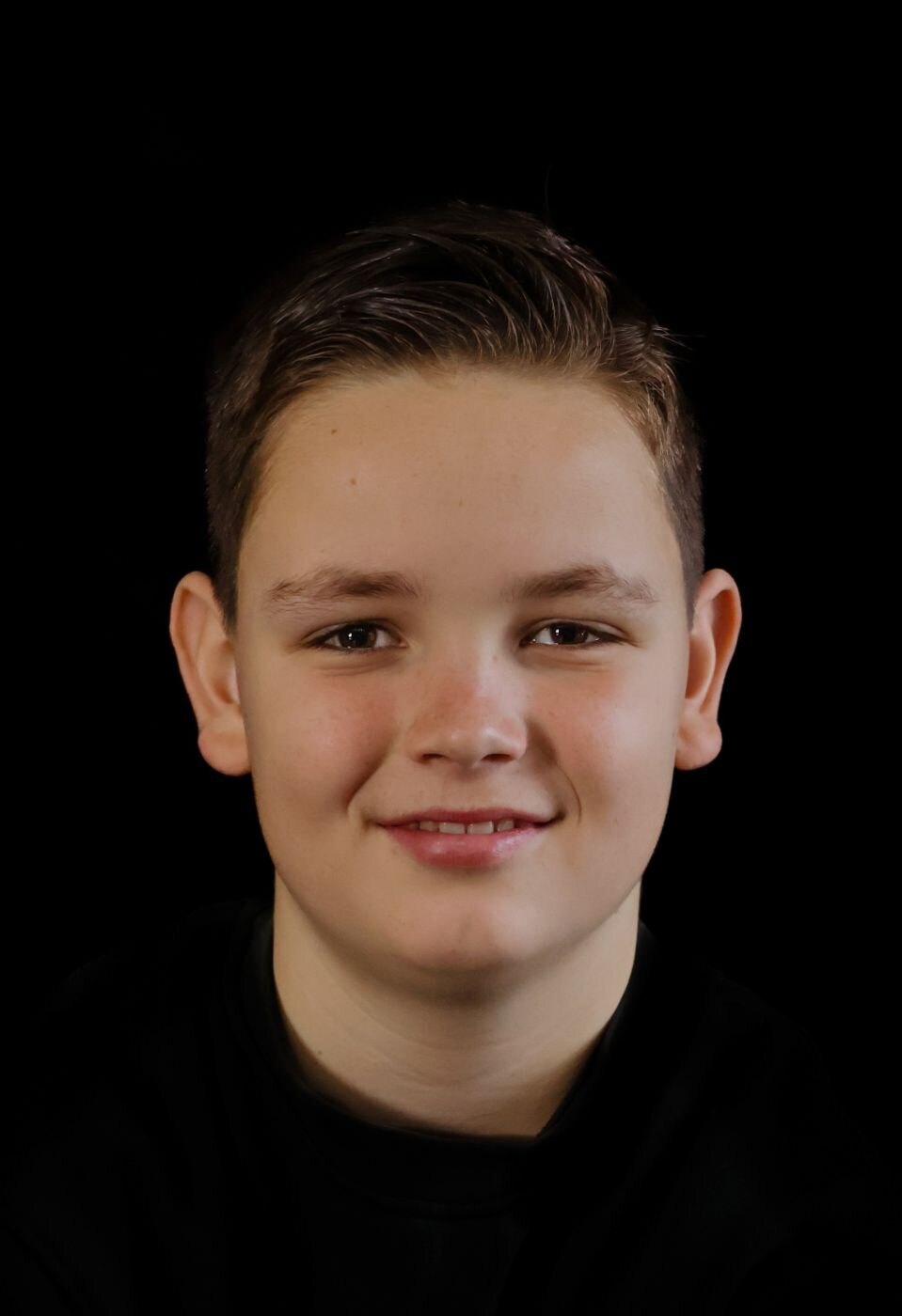 Een portretfoto van een tienerjongen met een open en vriendelijke uitstraling, gefotografeerd tegen een donkere achtergrond