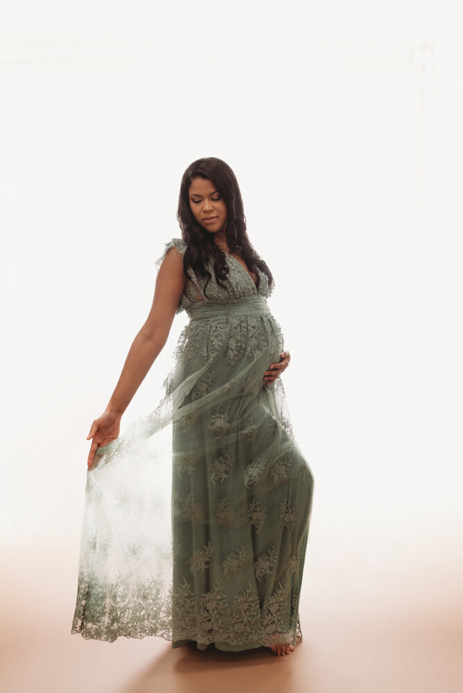 Maternity session with Atlanta, Georgia maternity photographer pregnant woman holding baby bump wearing siege green lace dress on white backdrop