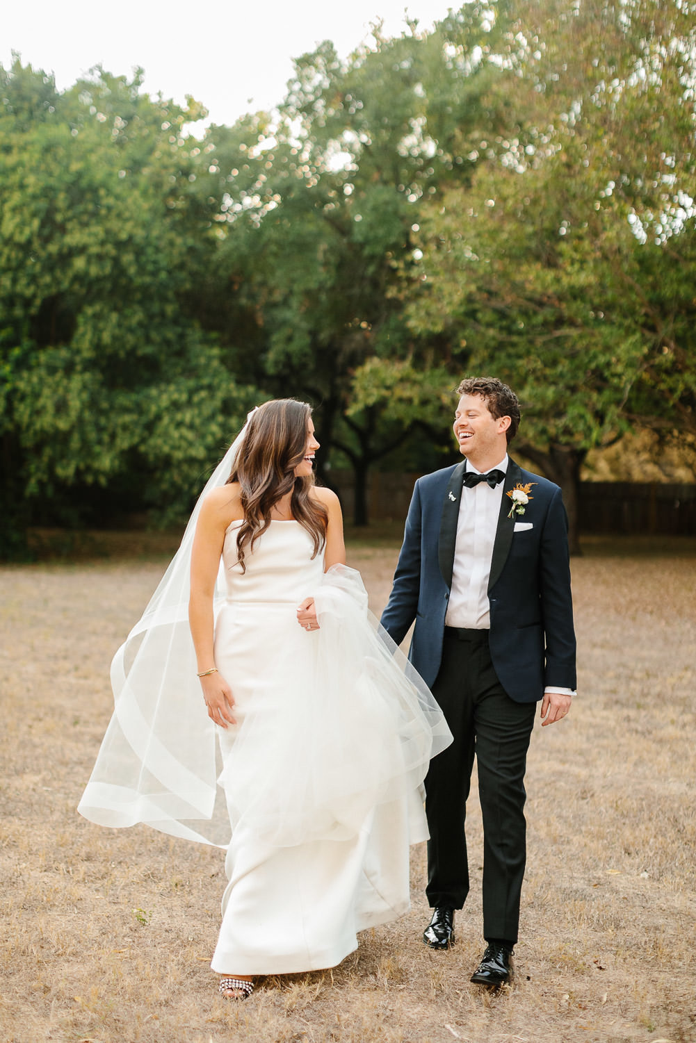 bride in white wedding dress smiling with groom wearing navy tuxedo walking at Matties wedding austin
