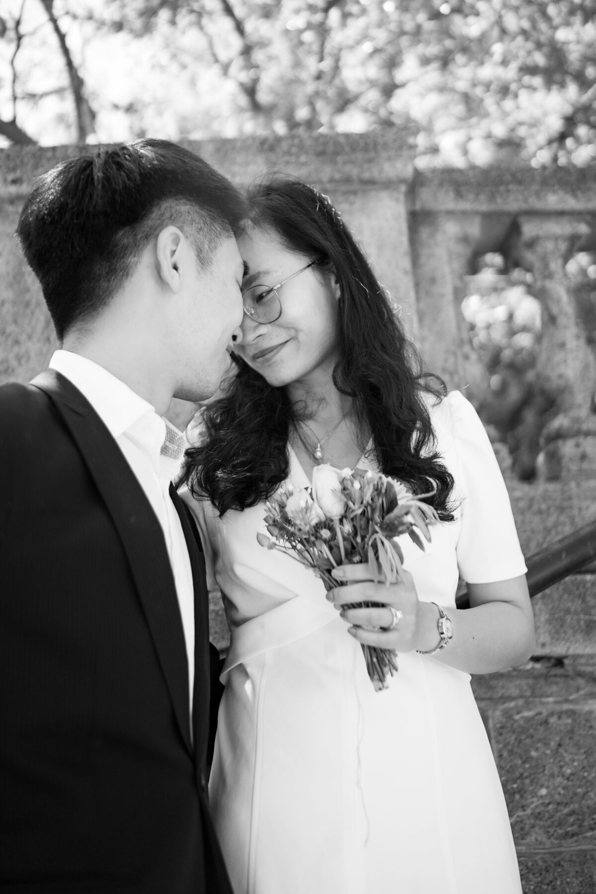 black and white image of a straight Asian couple touching foreheads in front of a stone wall