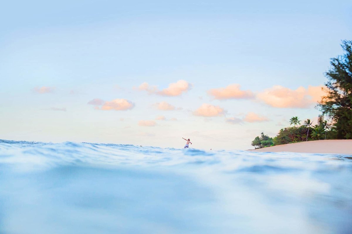 Abstract family portrait image photographed on Kauai Hawaii with young child running in the background and pretty pastel clouds with ocean in the foreground