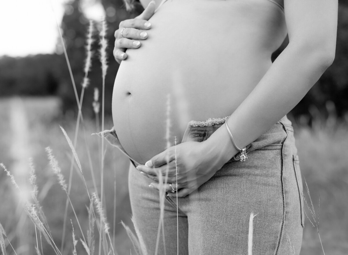 Artistic black and white close-up of pregnant belly with jeans unbuttoned in a Georgetown field