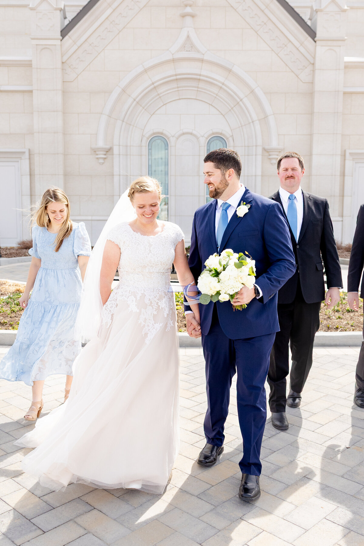 A close-up of the bride and groom holding hands and smiling at each other as they walk outside the temple.
