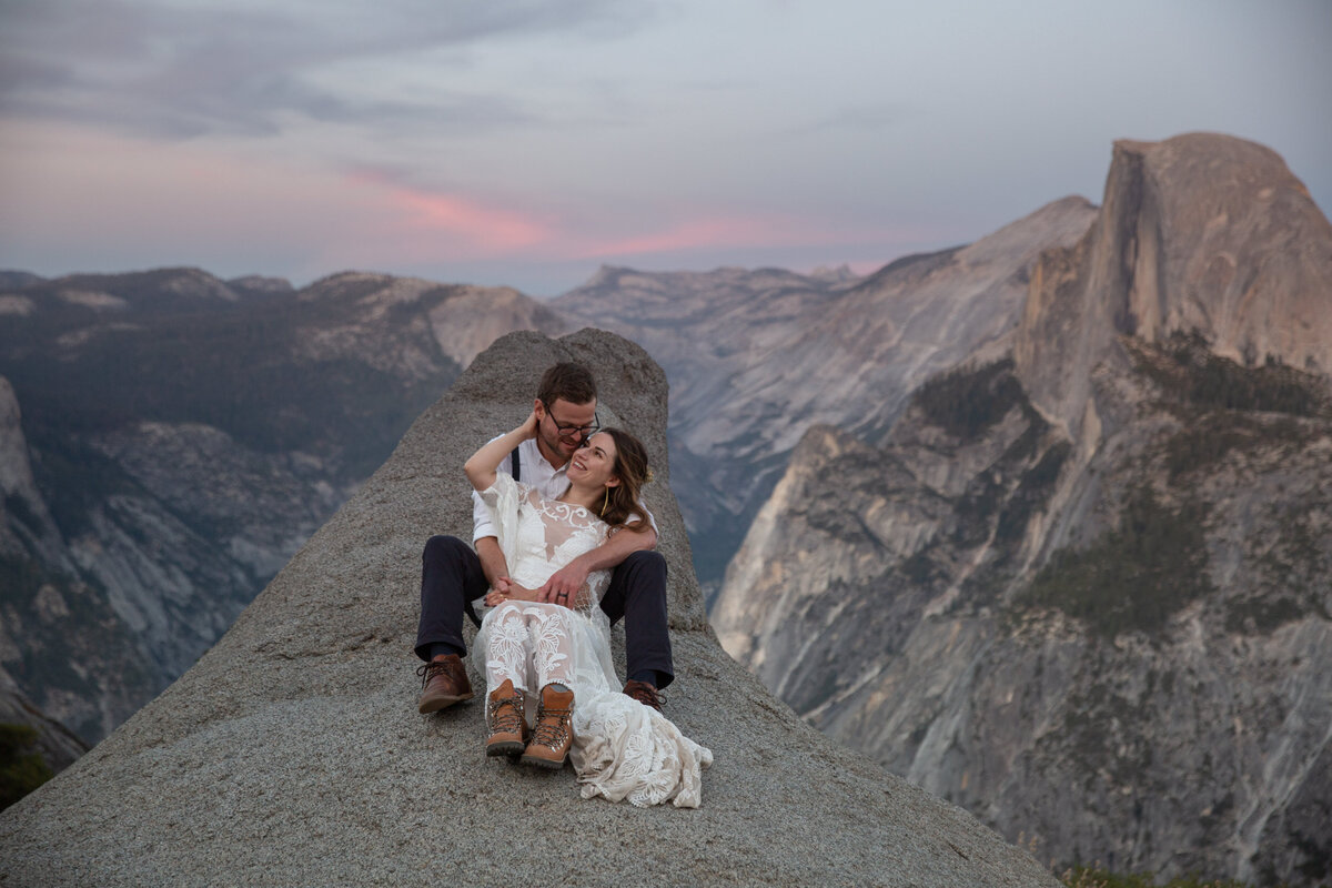 A bride sits between her grooms legs with her hands wrapped around his neck on their elopement day.