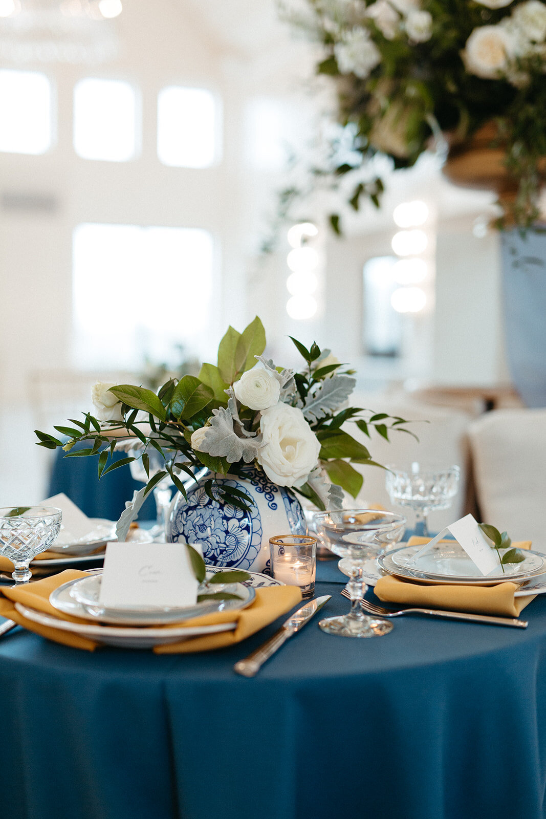 White place cards set on yellow napkin with white plates atop a table with blue line and florals.