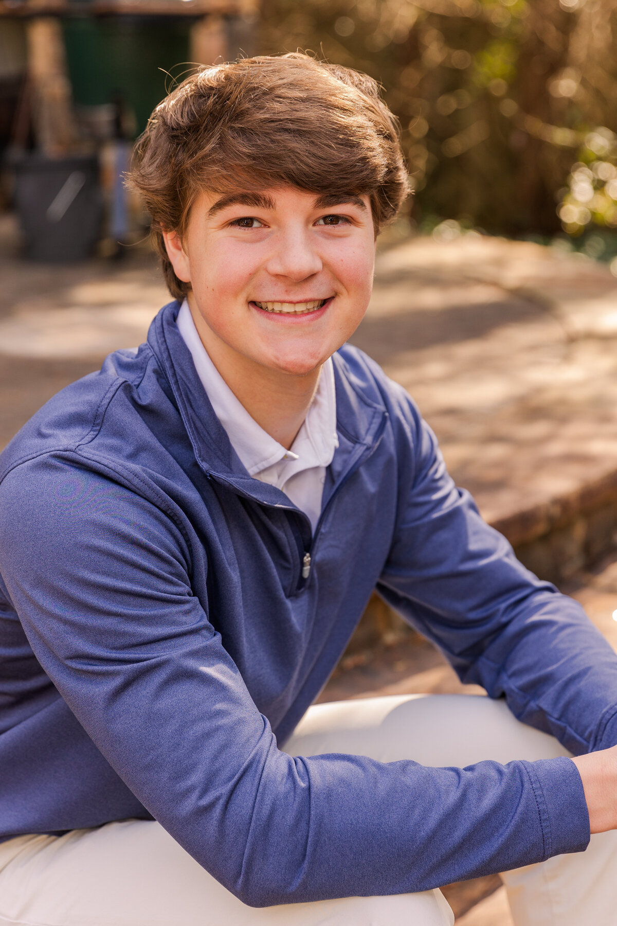 High school senior boy wearing white shirt and blue sweater sitting on stairs during Atlanta fall photoshoot Laure Photography