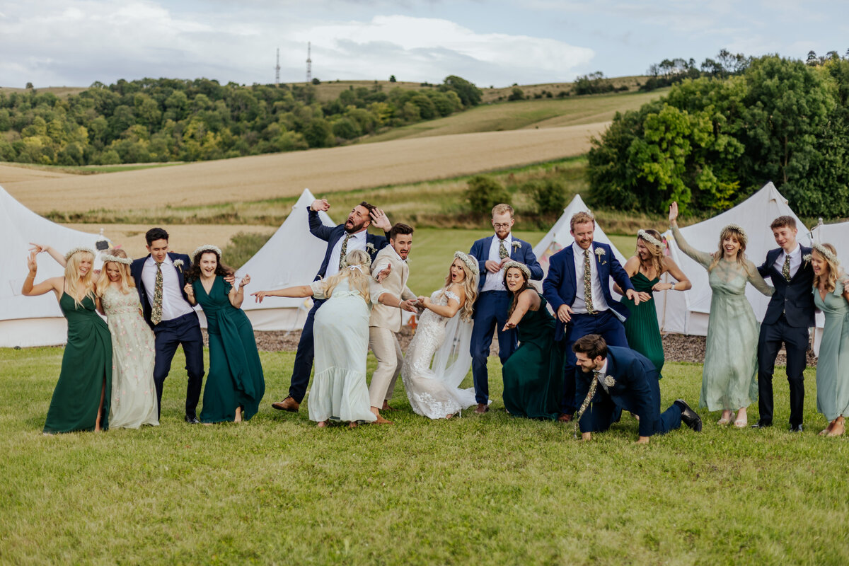A wedding crew stood together cheering while the bride sprays champagne towards the camera