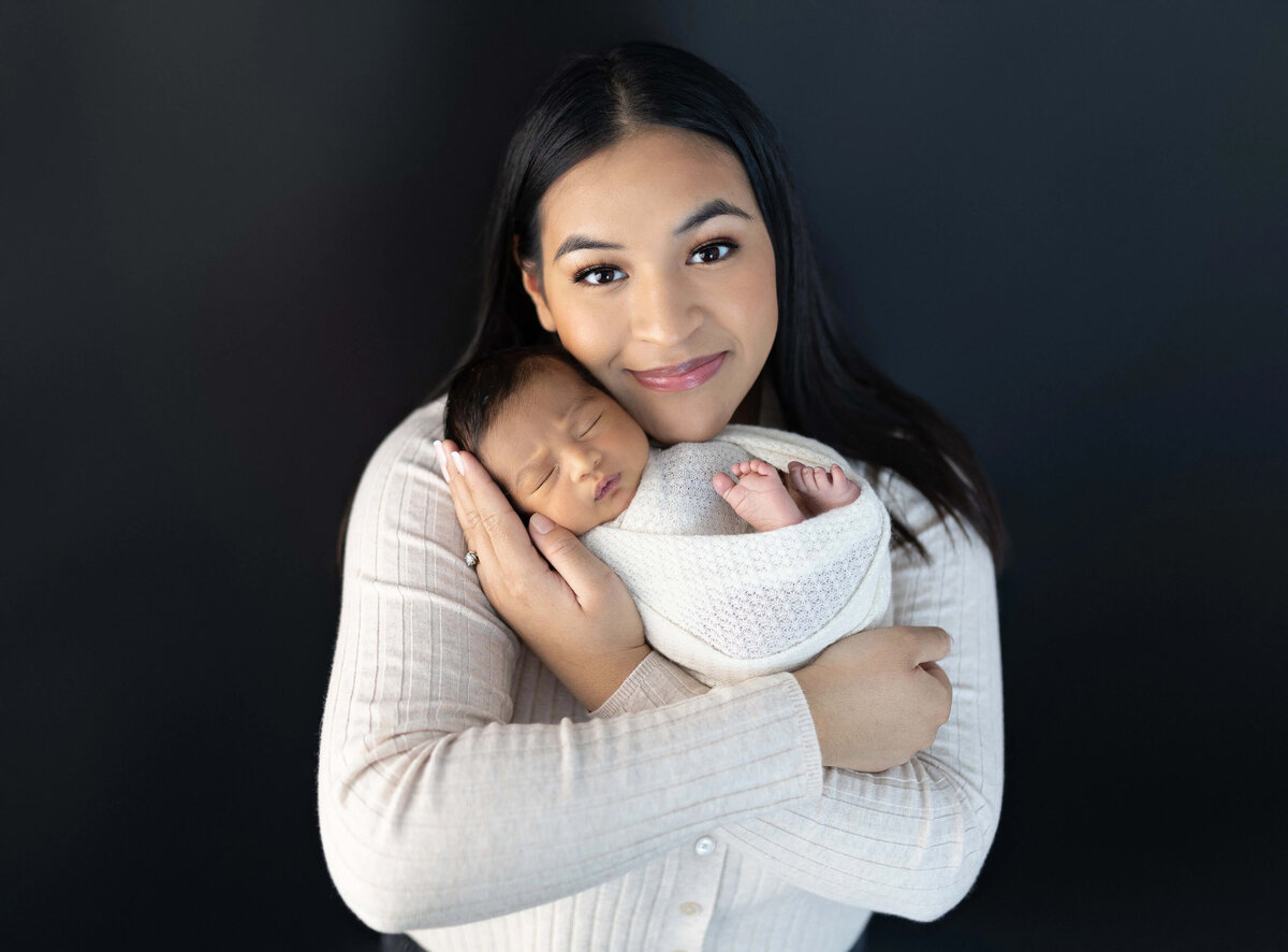 Mom holding sleeping newborn with soft smile - studio newborn portrait Minneapolis