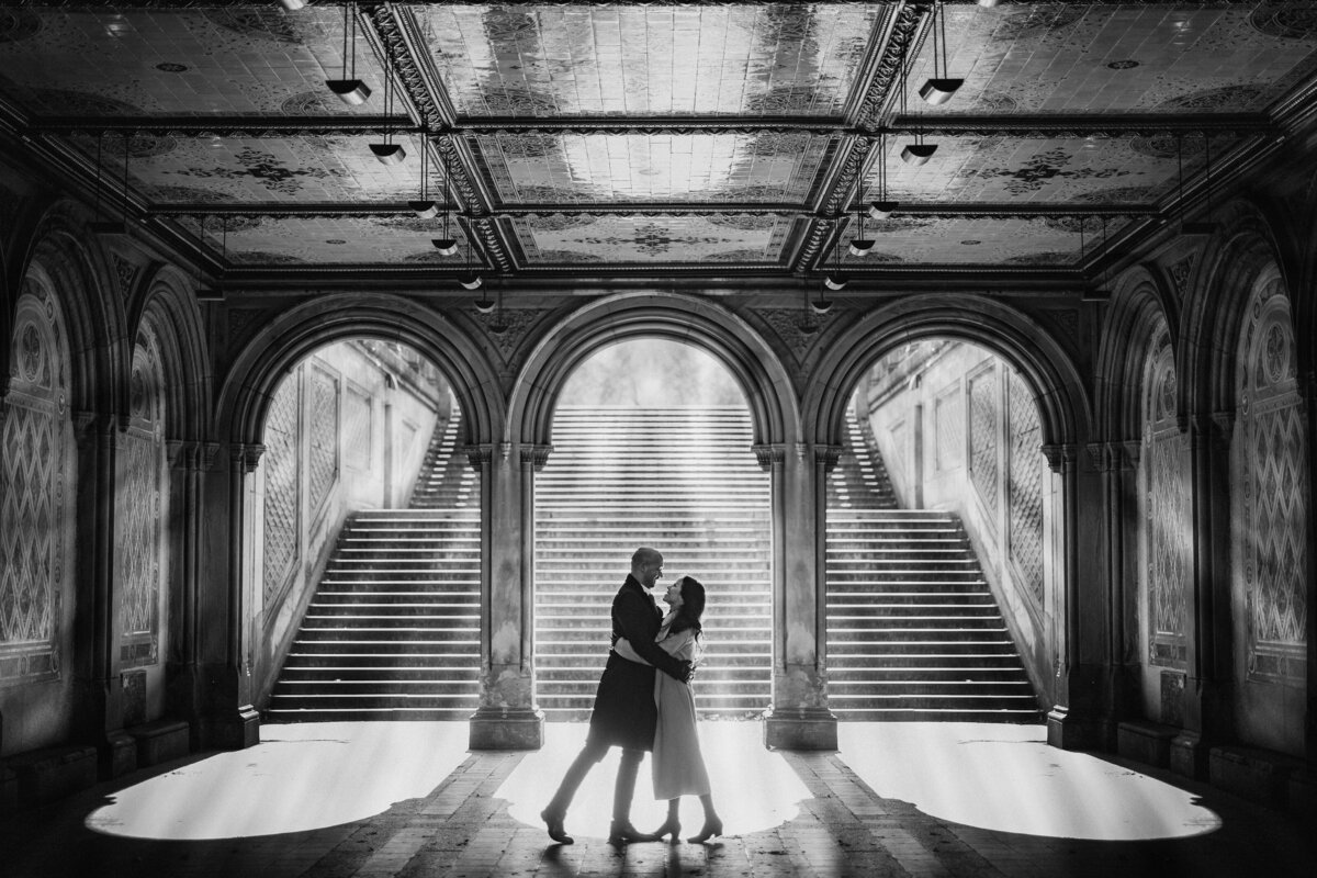 A couple hugging while standing at the bottom of a large staircase.