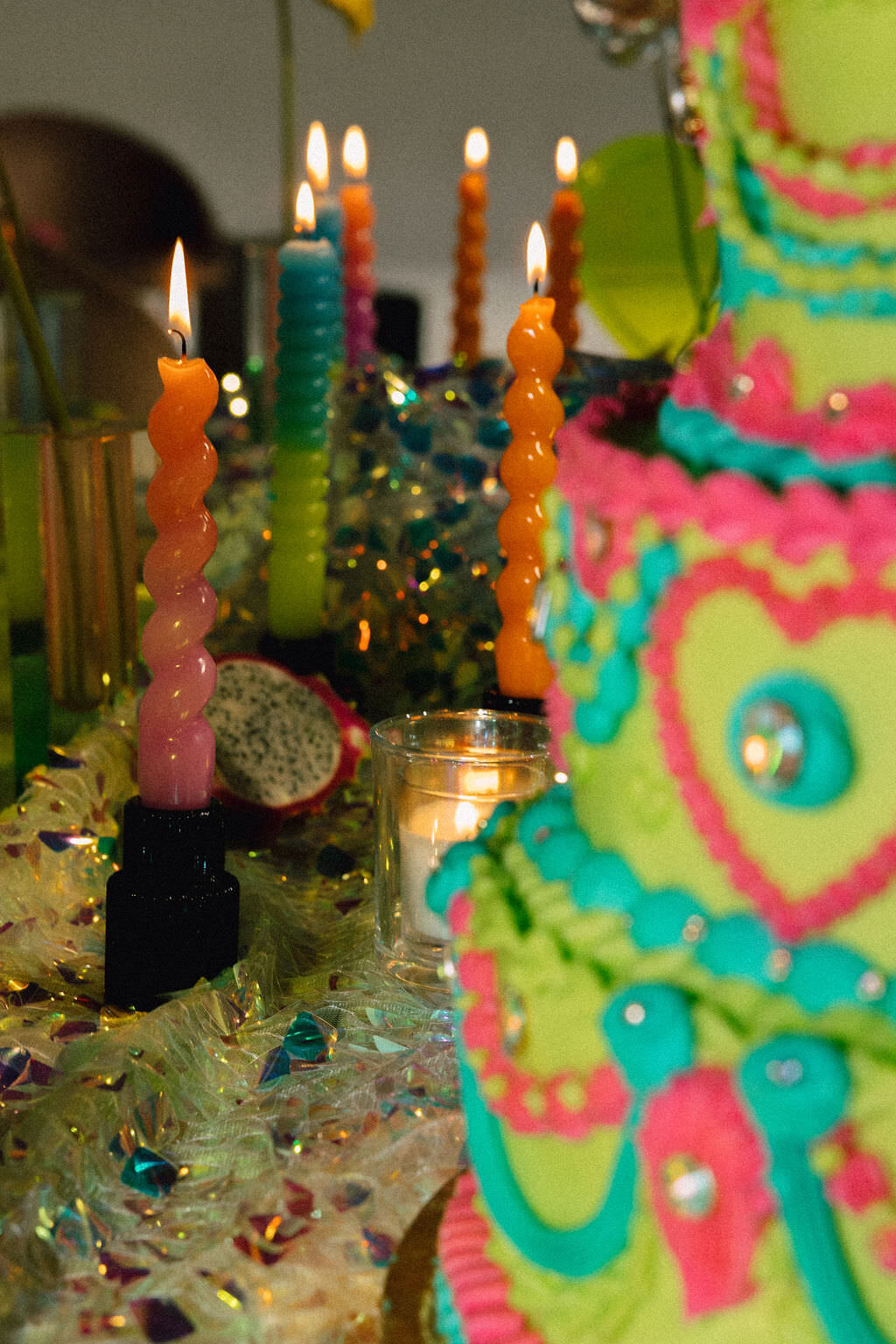 A colorful cake with colored candles on the table behind it.