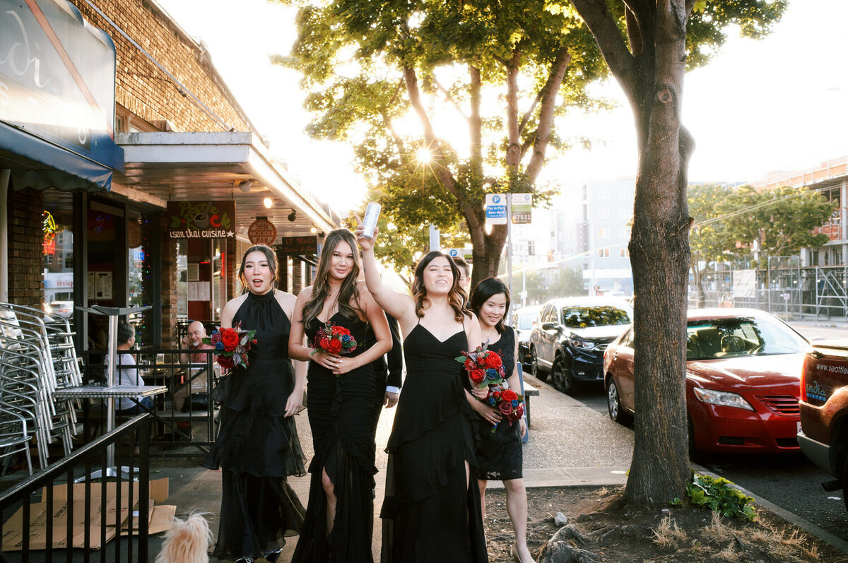 Bridesmaids laugh as they walk down a Seattle sidewalk with the sun setting