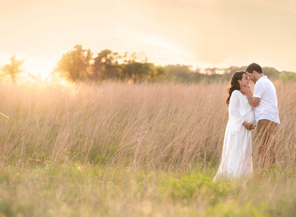 pregnant couple wearing white at sunset standing in a field of tall grass