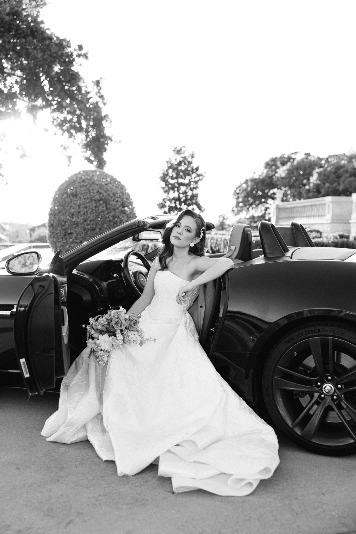 a bride posing in her wedding dress in the front seat of a car